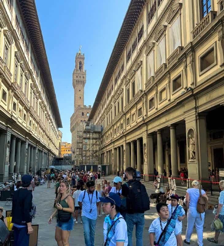 Crowds strolling through the courtyard of the Uffizi Gallery in Florence with Palazzo Vecchio visible in the background