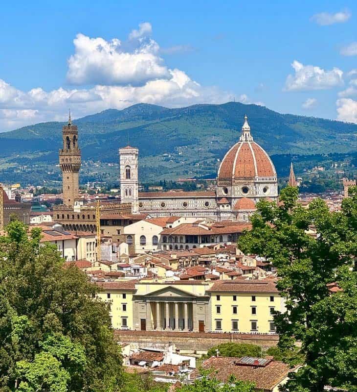 Panoramic view of Florence with the Cathedral of Santa Maria del Fiore (Duomo), Giotto’s Bell Tower, and Palazzo Vecchio under a bright blue sky.