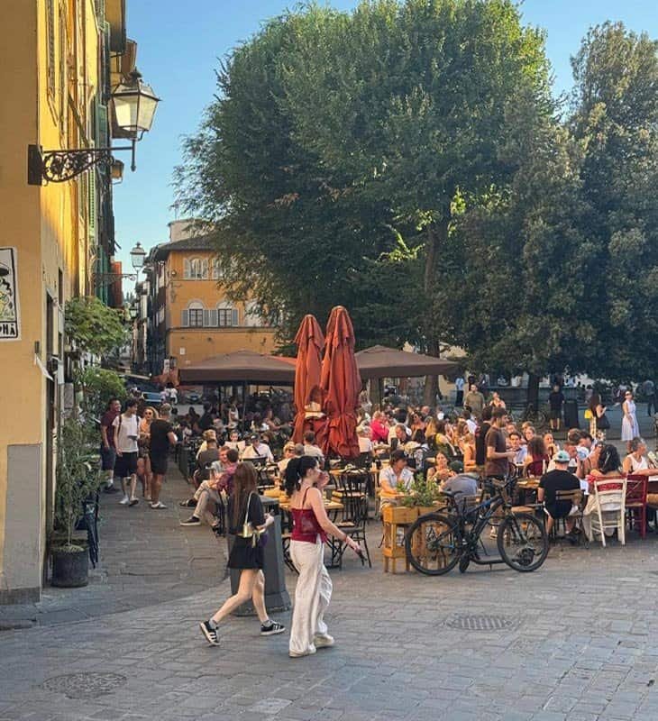  Lively outdoor café scene in Piazza Santo Spirito, Florence, with people dining and walking in the early evening.