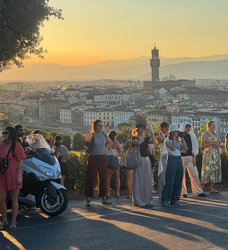  Tourists enjoying sunset views over Florence from Piazzale Michelangelo, with Palazzo Vecchio silhouetted in the background.