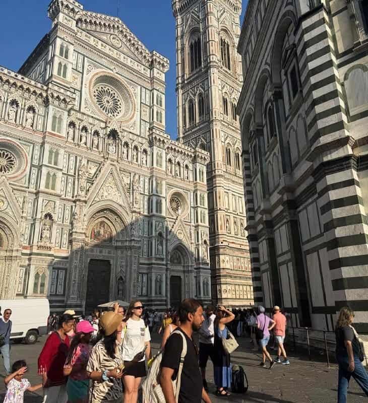 People walking in front of the richly decorated façade of Florence’s Cathedral (Duomo) with Giotto’s Bell Tower rising beside it.